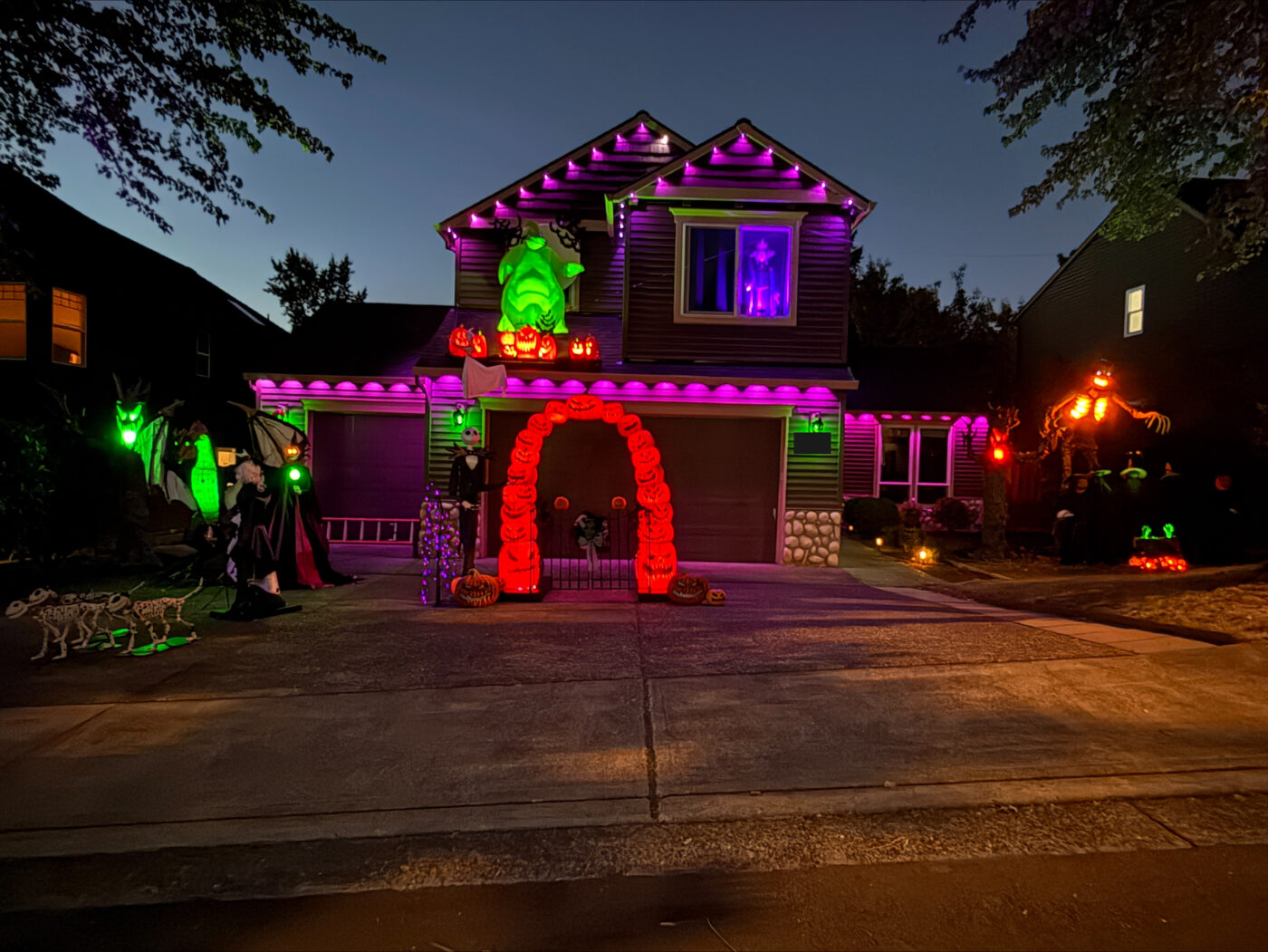 A purple-lit house with a giant Oogie Boogie, a glowing pumpkin arch and Jack Skellington at dusk